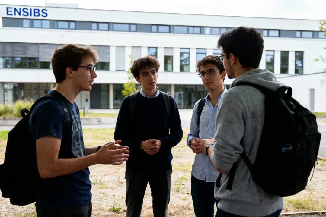 Quatre étudiants discutent à l'extérieur d'un bâtiment ENSIBS. Ils portent des sacs à dos.