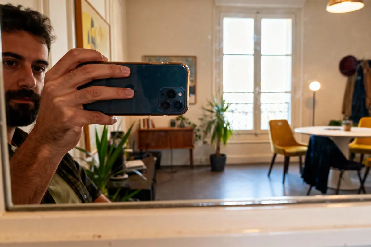 Un homme prend un selfie dans un miroir, intérieur lumineux avec plantes et mobilier moderne.