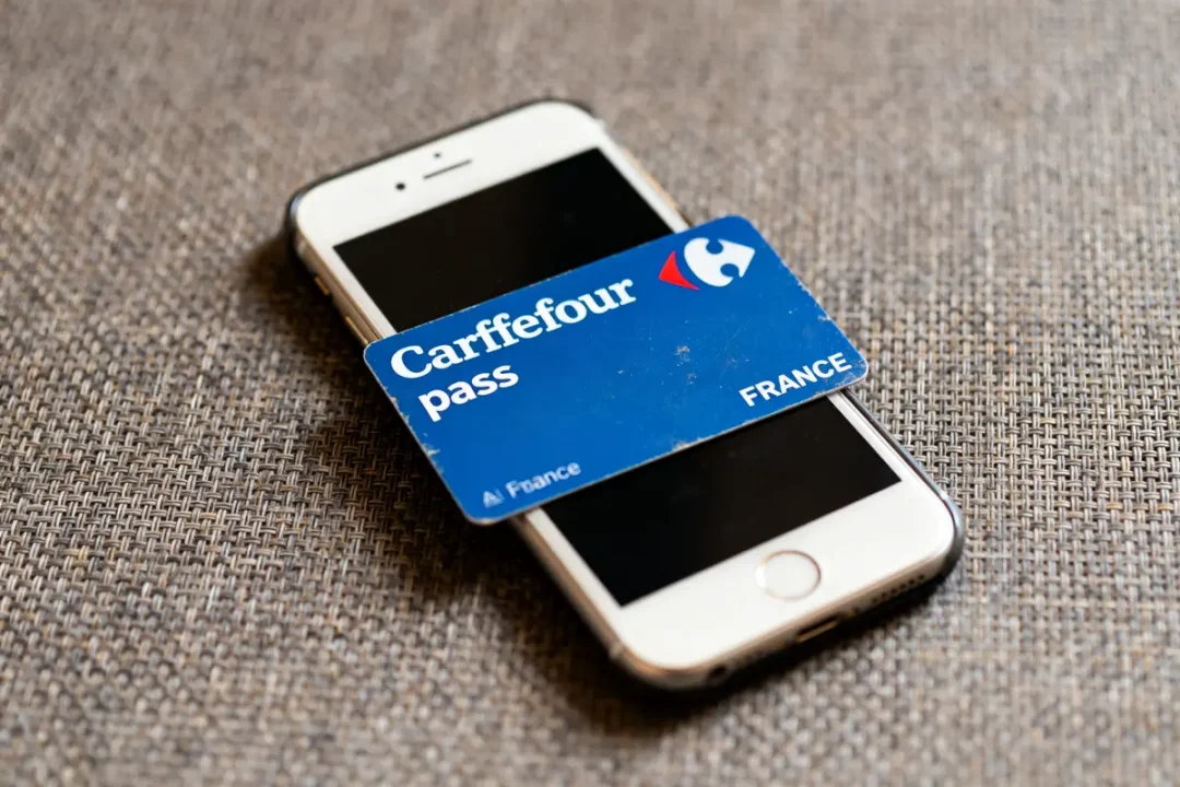 Carte Pass Carrefour posée sur un téléphone sur fond de textile marron