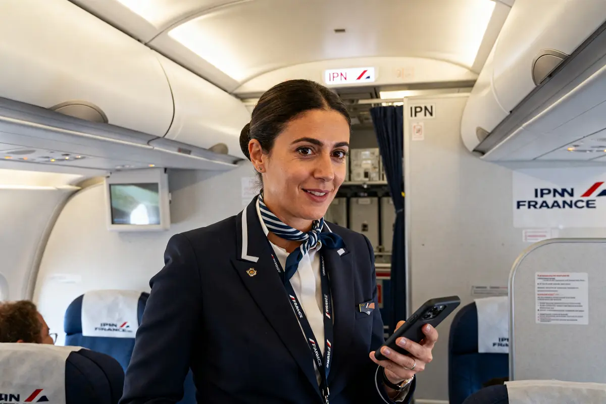 Hôtesse de l'air souriante avec téléphone à bord d'un avion IPN Air France