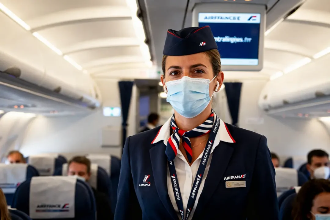 Hôtesse de l'air masquée dans un avion intralignes.airfrance.fr servant les passagers à bord