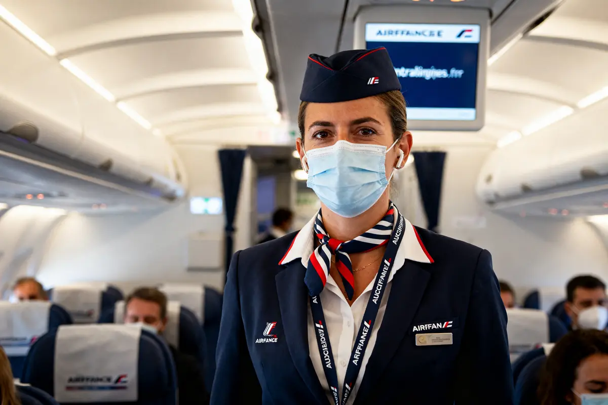 Hôtesse de l'air masquée dans un avion intralignes.airfrance.fr servant les passagers à bord