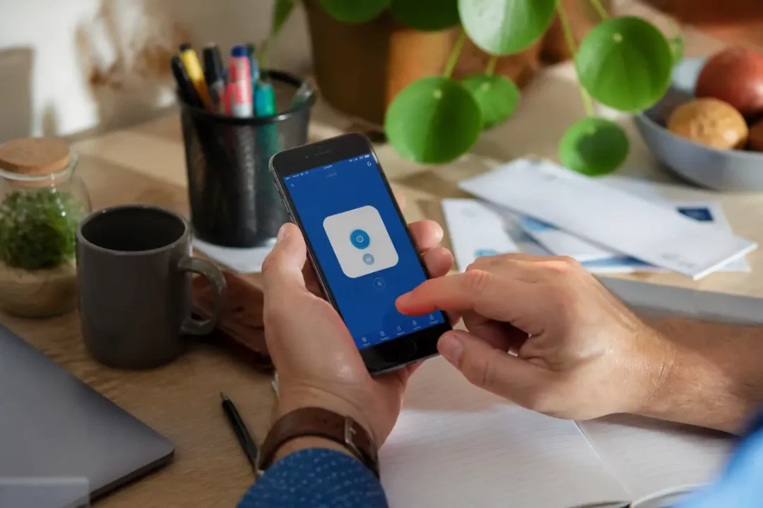 Main tenant un smartphone avec application Certicode Plus sur un bureau organisé