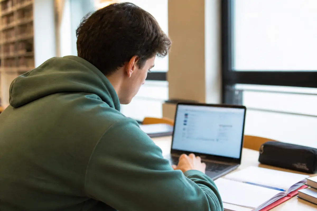 Étudiant utilisant ENT UBS Lorient sur ordinateur portable en bibliothèque universitaire.