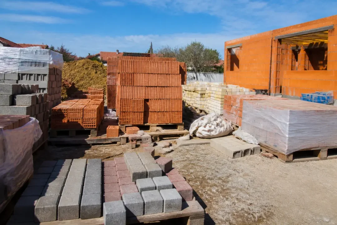 Matériaux de construction empilés : briques, pavés et parpaings sur chantier ensoleillé.