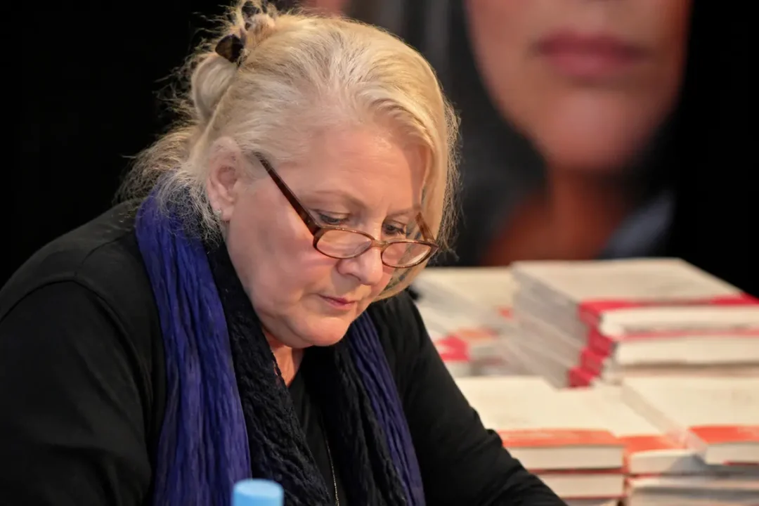 Josiane Balasko signant des livres entourée d'ouvrages, suggérant la fortune de Josiane Balasko