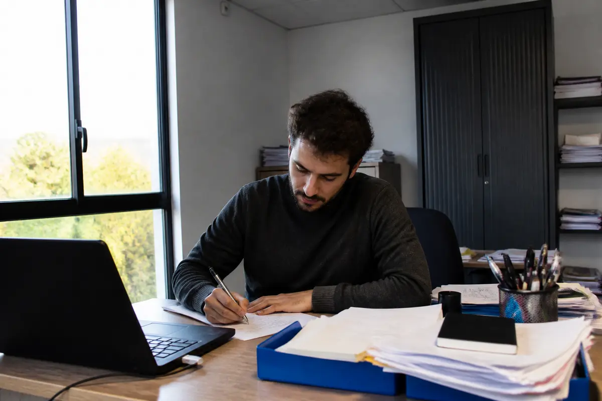Homme écrivant à un bureau, préparation à une rupture anticipée de CDD par le salarié