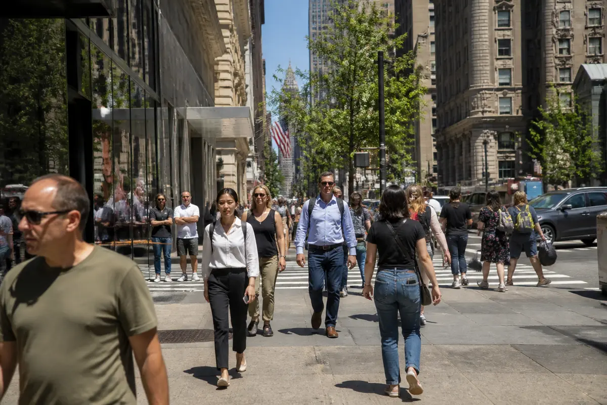 Des passants marchent dans une rue animée de New York, discutant du salaire moyen local